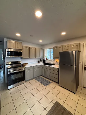 Kitchen with recessed lighting, tile flooring, light-toned cabinetry, stainless steel appliances, and solid surface countertops