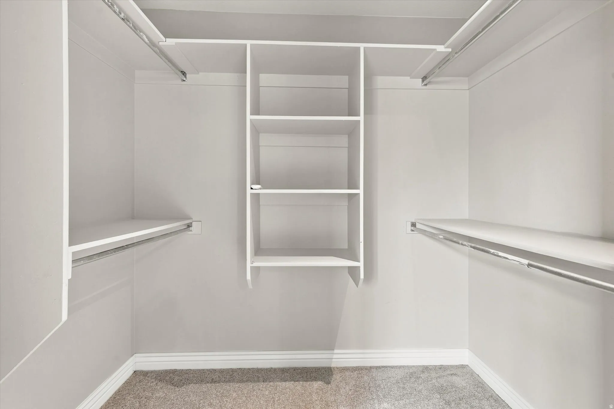 Walk-in closet featuring white built-in shelving, multiple hanging rods, and carpet flooring