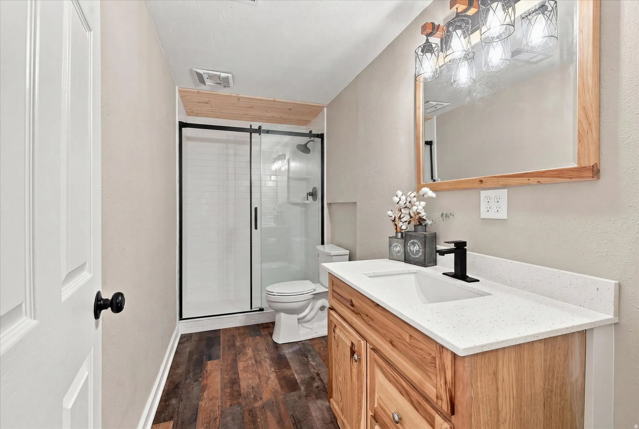 Bathroom featuring wood-finish flooring, a wood vanity with a white countertop and integrated sink, a matte black faucet, and a mirror with a wood frame