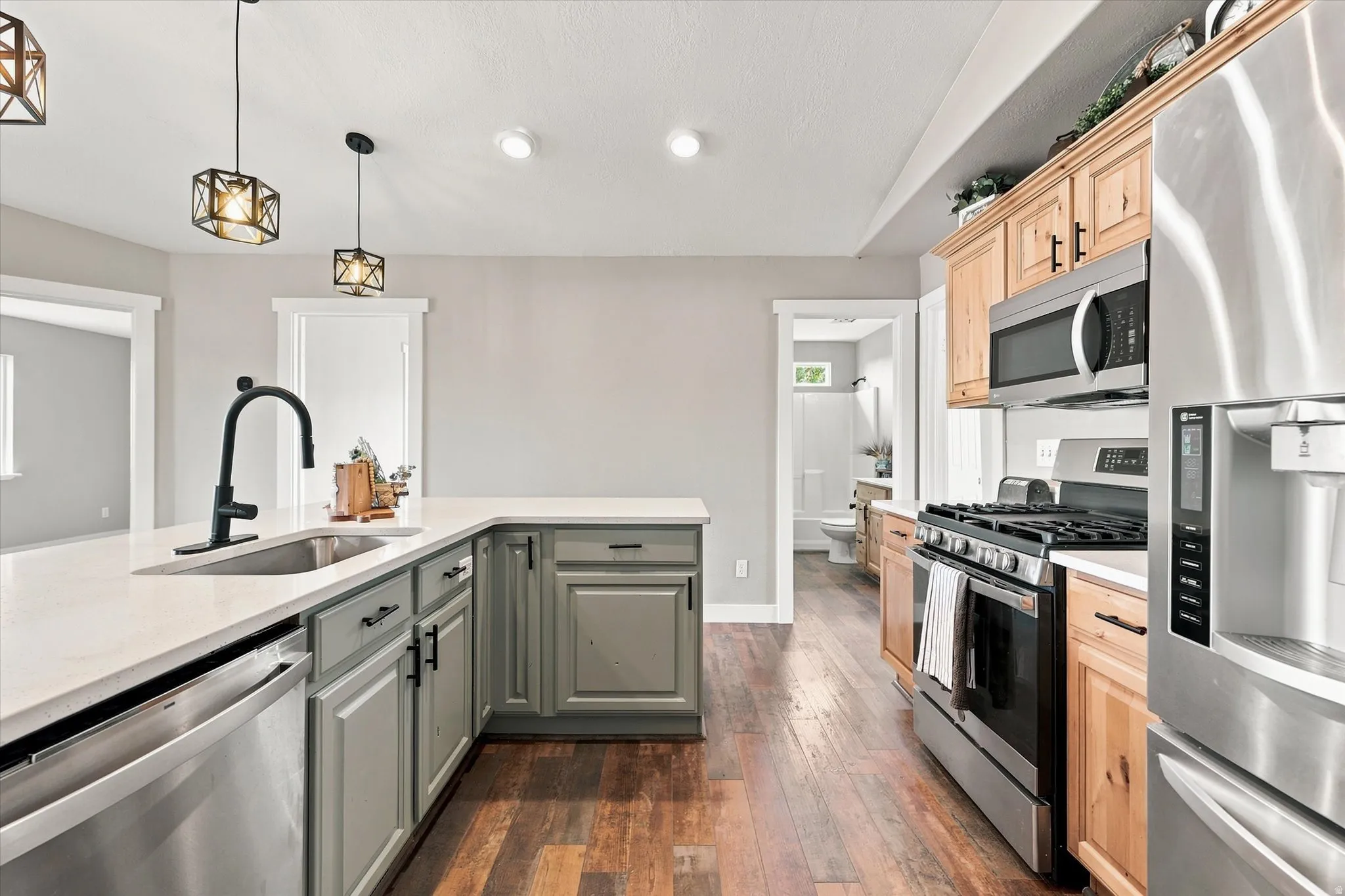 Modern kitchen featuring stainless steel appliances, wood-finish flooring, light gray cabinetry, and a large L-shaped countertop with an undermount sink and matte black faucet