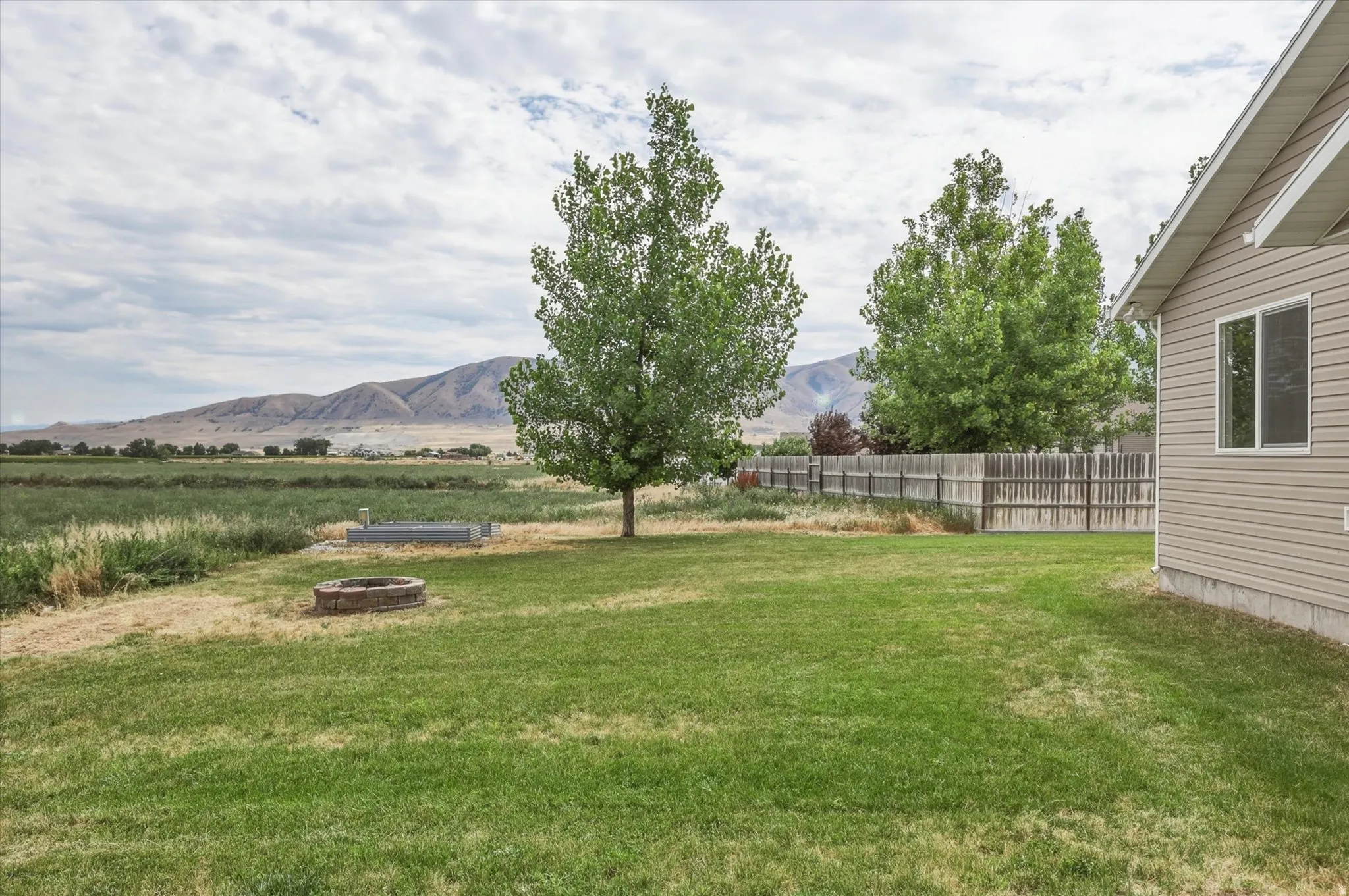 Expansive lawn featuring a built-in fire pit, mature trees, and a wood fence