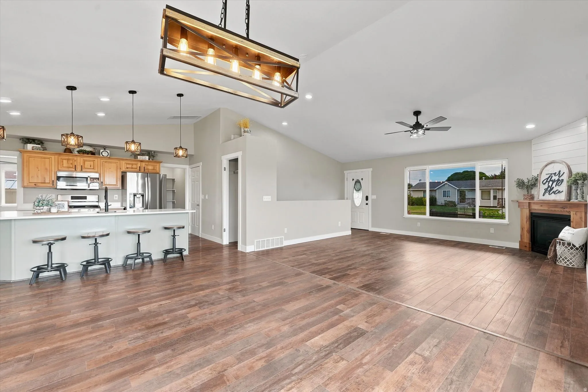 Open-concept living area with wood-finish flooring, vaulted ceiling, and a fireplace featuring a wood mantel