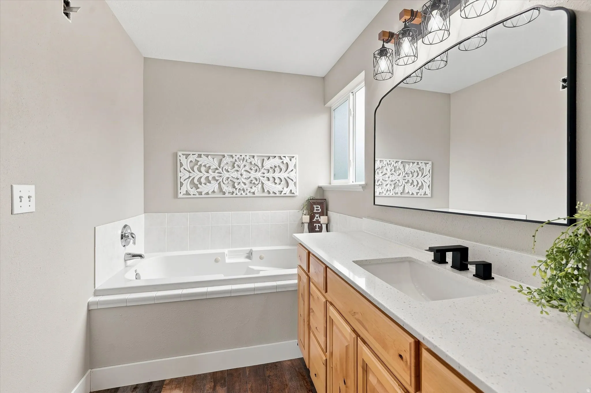 Bathroom featuring a built-in jetted tub, wood-finish vanity with ample storage, a white countertop, and a large wall-mounted mirror