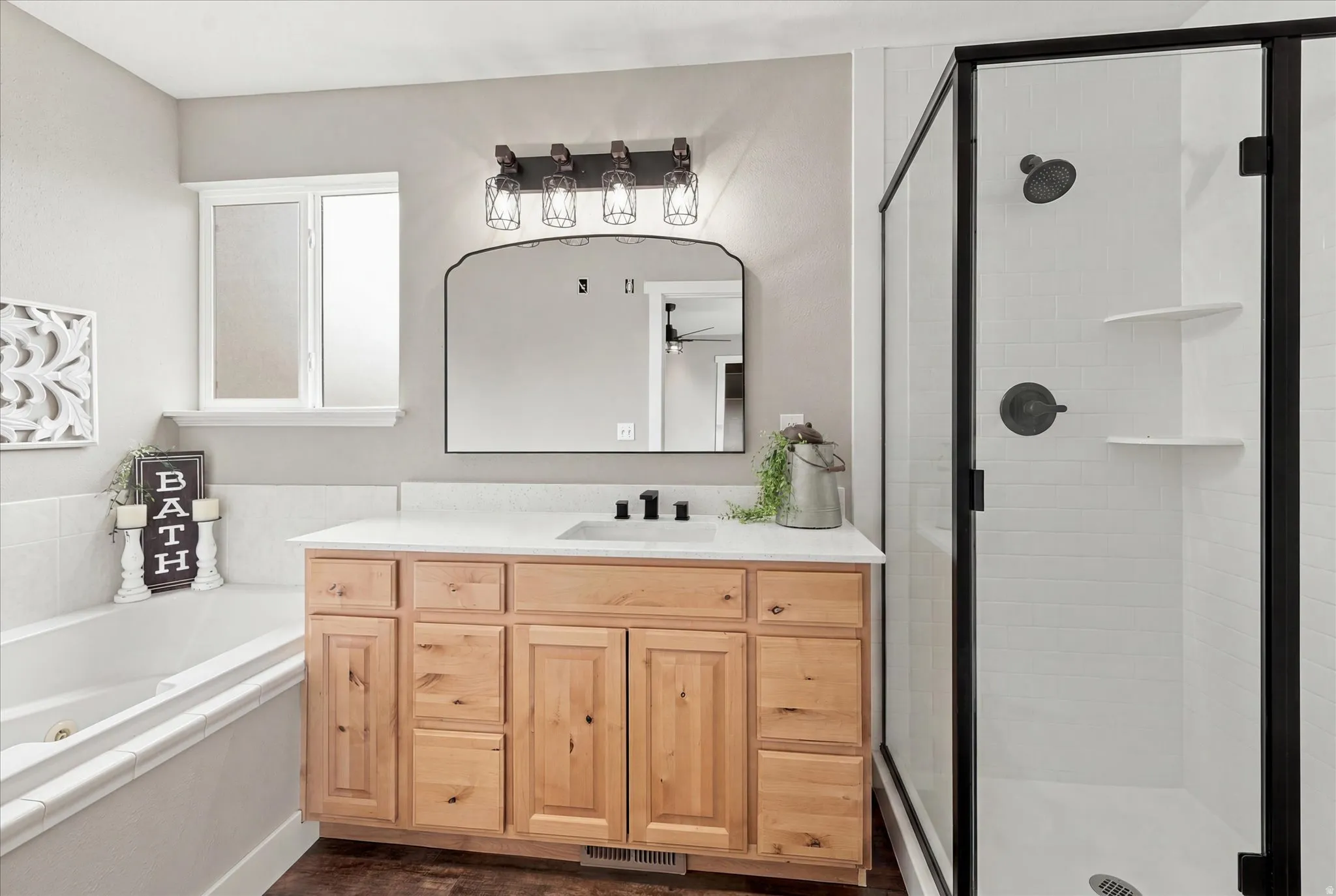 Bathroom featuring a natural wood-finish vanity with a light-toned countertop, a shower enclosure with dark-framed glass, a soaking tub, and dark-finish hardware throughout