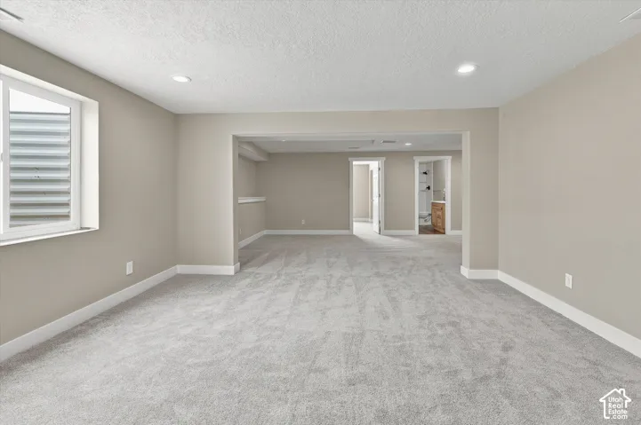 Spacious room featuring light gray carpet, neutral wall tones, white trim, recessed lighting, and a white-framed window
