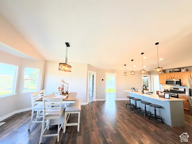 Vaulted ceilings, wood-finish flooring, kitchen island with seating, stainless steel appliances, and pendant lighting