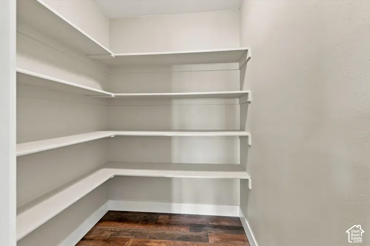 Pantry featuring extensive built-in shelving, wood-finish flooring, and light-toned walls