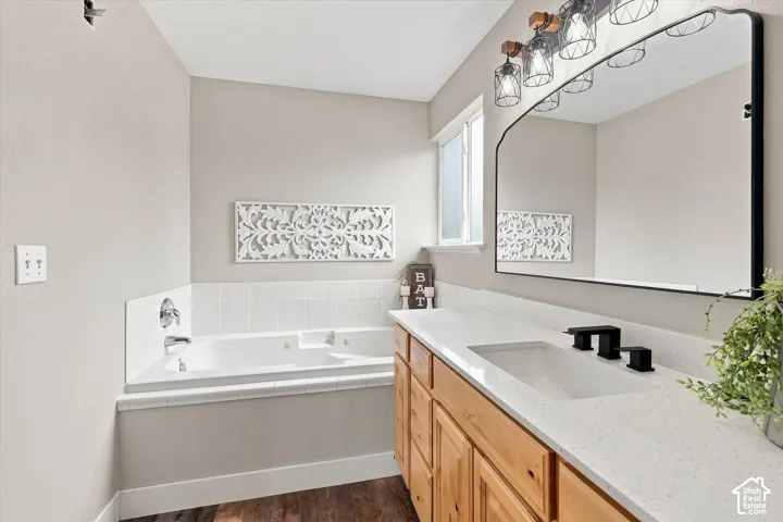 Bathroom featuring a built-in jetted tub, wood-finish vanity with ample storage, a white countertop, and a large wall-mounted mirror