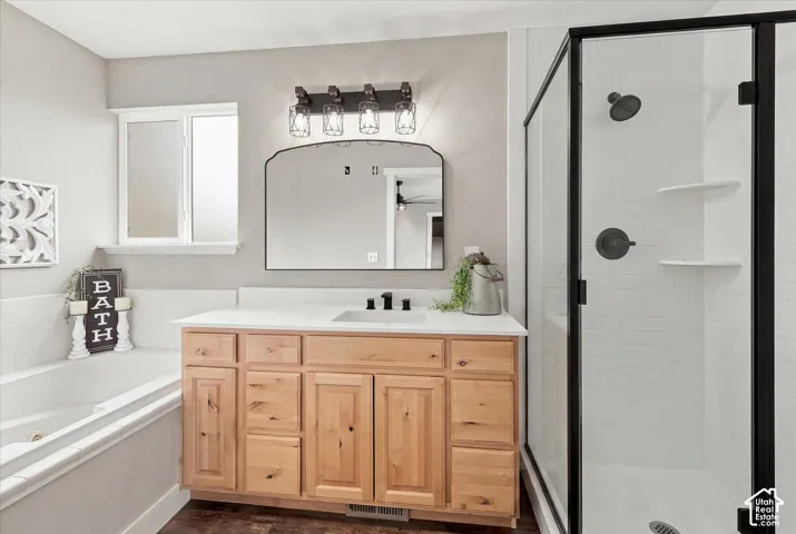 Bathroom featuring a natural wood-finish vanity with a light-toned countertop, a shower enclosure with dark-framed glass, a soaking tub, and dark-finish hardware throughout