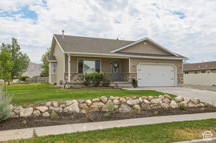 Single-story residence featuring a two-car garage, stone and siding exterior, a concrete driveway, and a front rock garden with shrubbery
