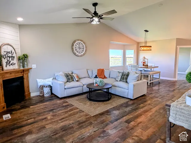 Vaulted ceiling with a ceiling fan, wood-finish flooring, built-in fireplace with a wood mantle, shiplap accent wall, and a bay window