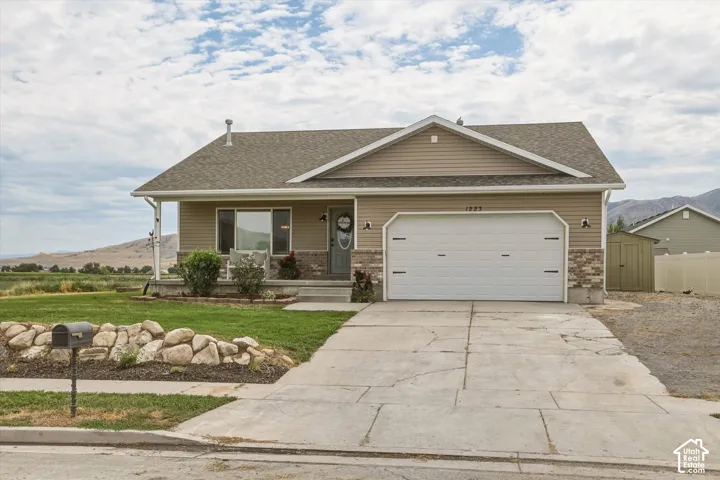 Light-toned siding exterior with a contrasting gray front door, an attached two-car garage, stone-accented foundation, and a covered porch entry
