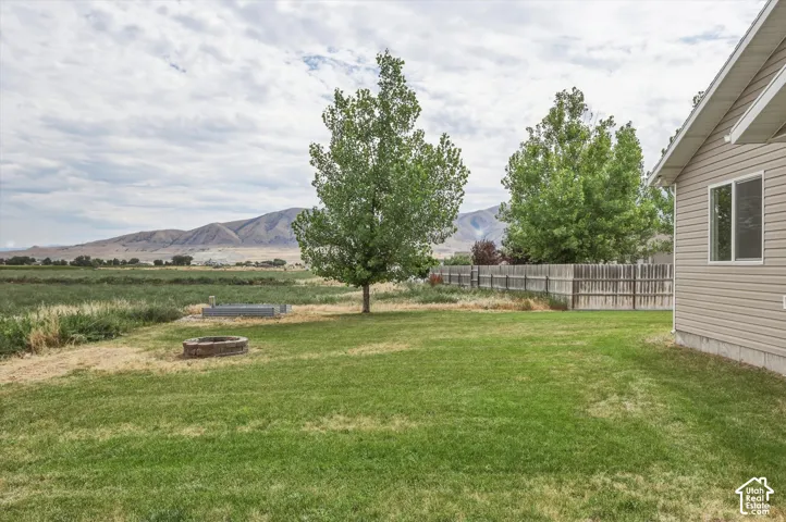 Expansive lawn featuring a built-in fire pit, mature trees, and a wood fence