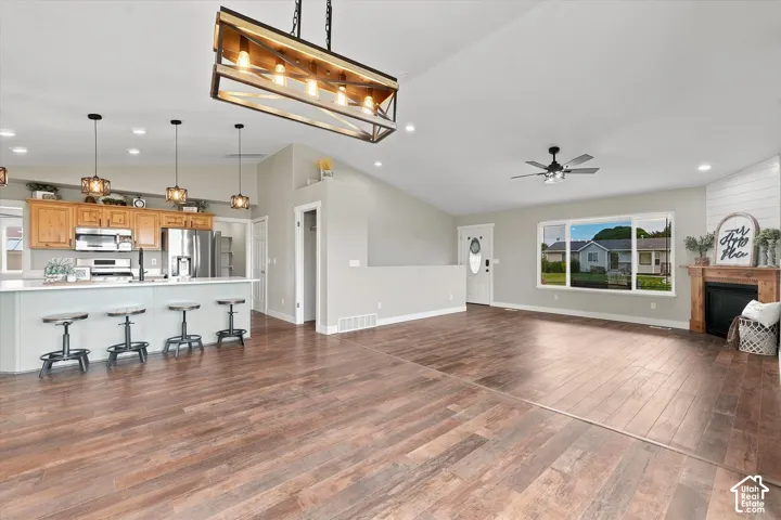 Open-concept living area with wood-finish flooring, vaulted ceiling, and a fireplace featuring a wood mantel