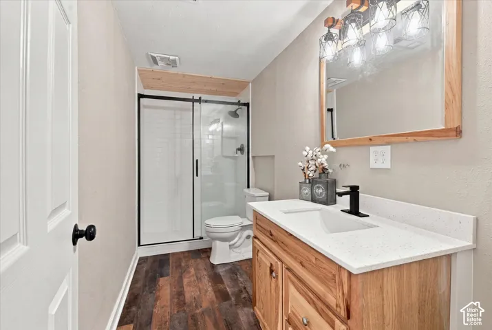 Bathroom featuring wood-finish flooring, a wood vanity with a white countertop and integrated sink, a matte black faucet, and a mirror with a wood frame