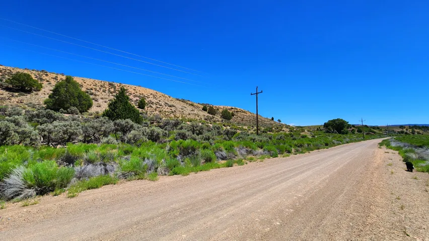 Expansive open terrain with a clear sky backdrop, featuring a gravel road, power lines, and natural vegetation