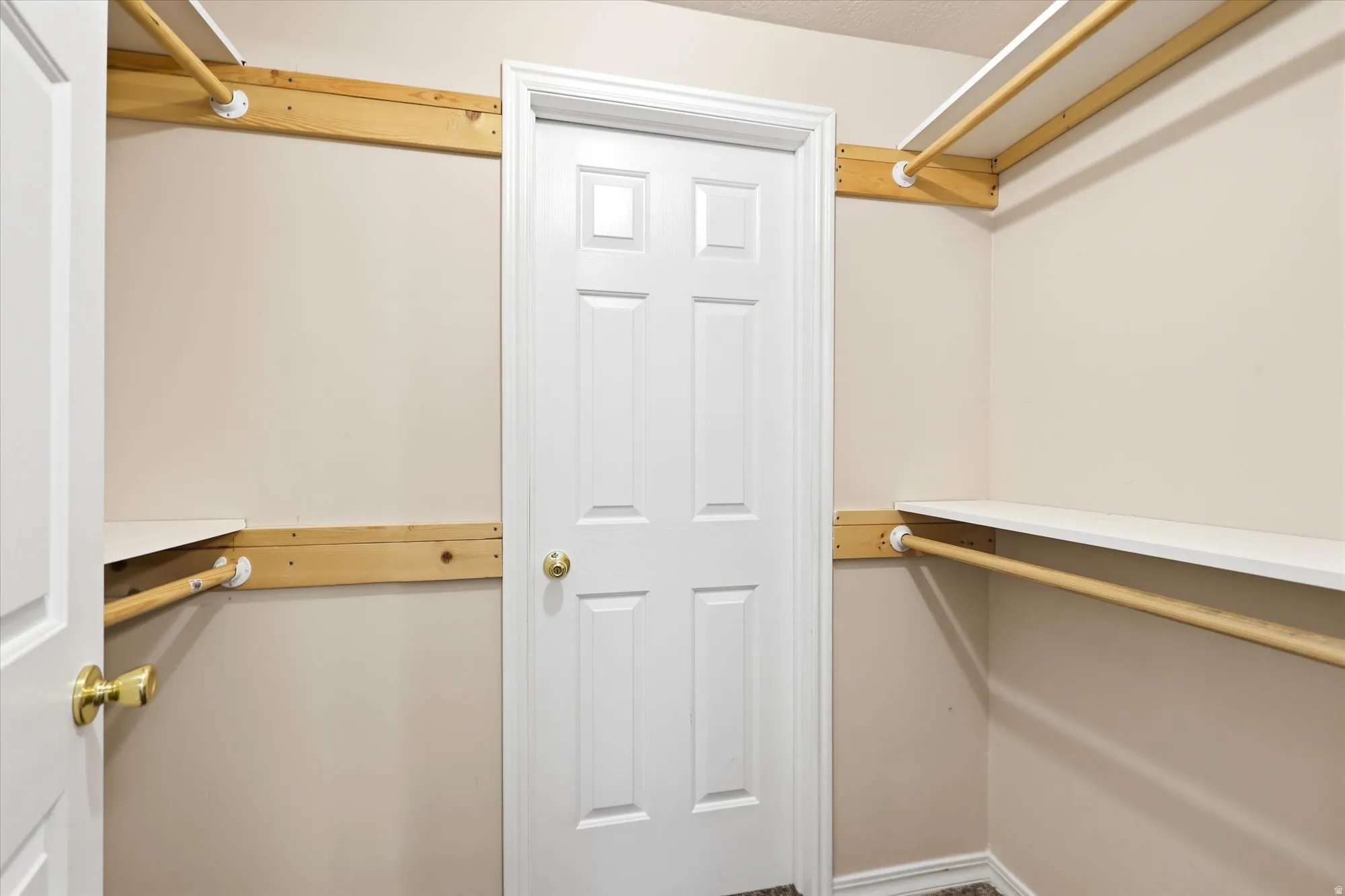 Walk-in closet with four shelves and hanging rods. White door enters into a second closet/room for additional storage, a sewing/craft room, etc.