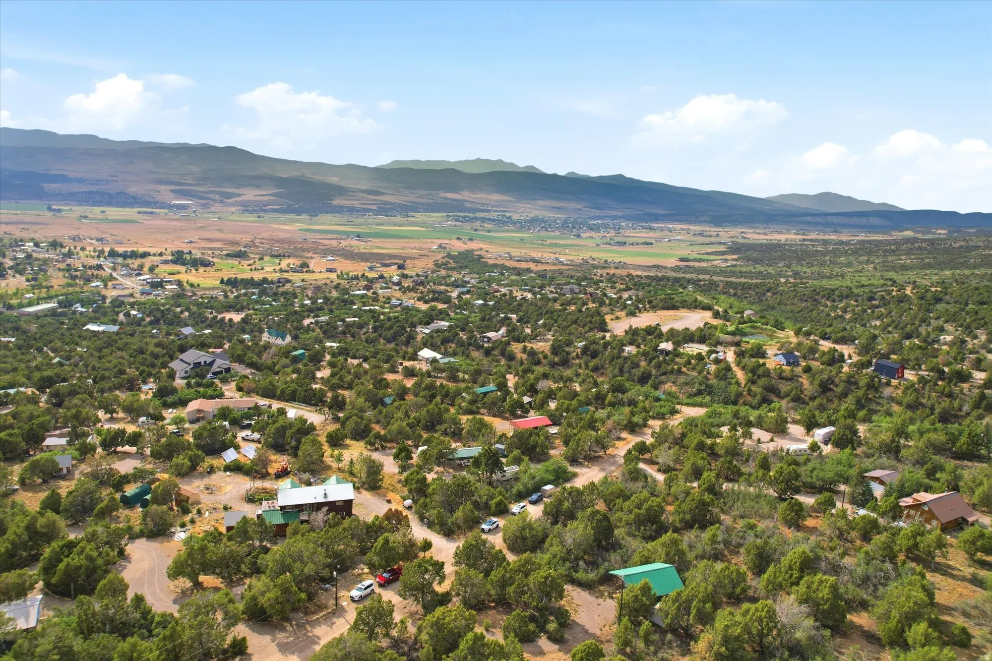 Expansive aerial southwest perspective showcasing the residential area with abundant mature trees and mountainous terrain in the distance