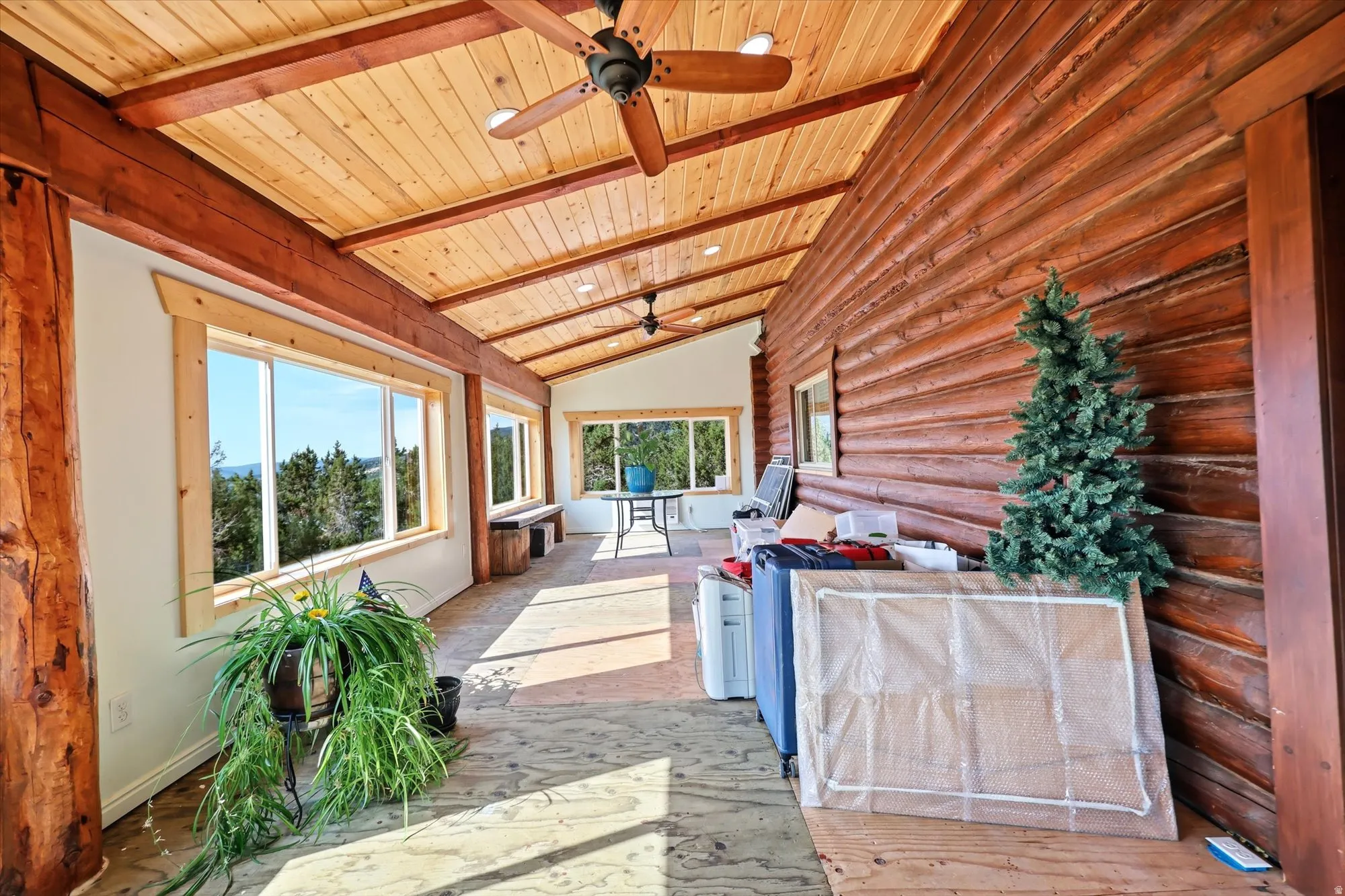 Spacious sunroom featuring extensive log siding, exposed timber beams, wood ceiling, multiple picture windows, and ceiling fans