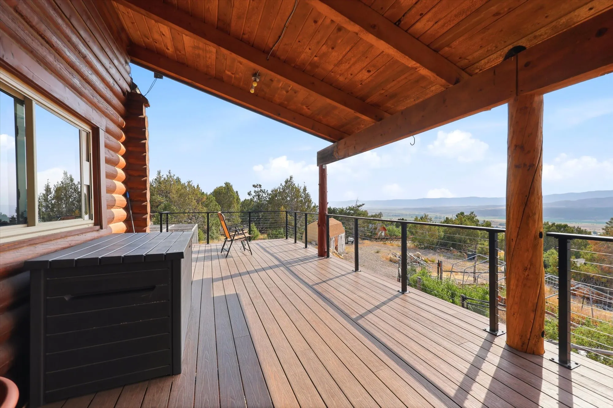 Expansive outdoor deck featuring Trex flooring, a covered ceiling with wood beams, and log column supports