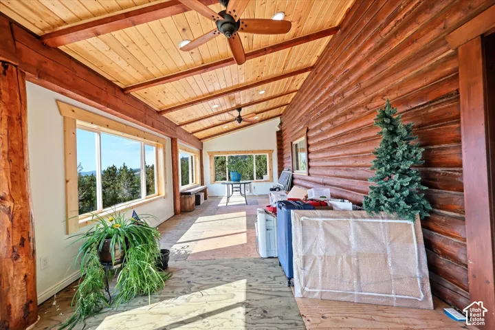 Spacious sunroom featuring extensive log siding, exposed timber beams, wood ceiling, multiple picture windows, and ceiling fans