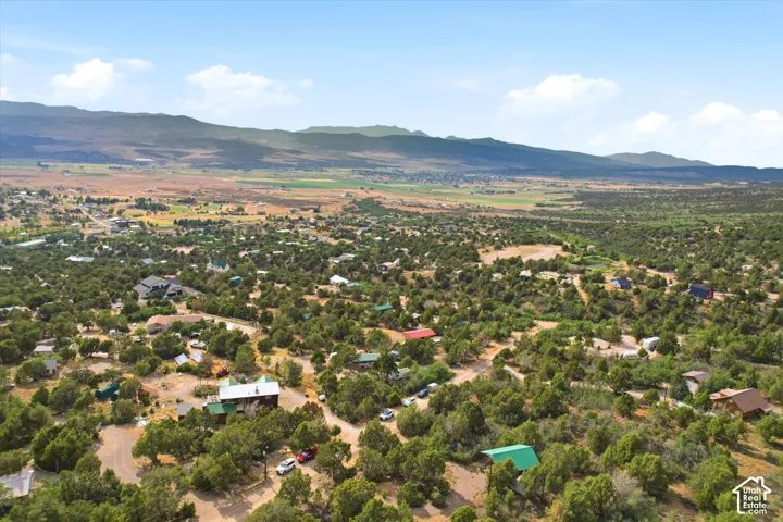 Expansive aerial southwest perspective showcasing the residential area with abundant mature trees and mountainous terrain in the distance