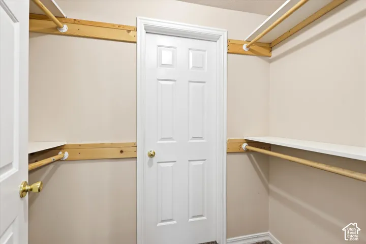 Walk-in closet with four shelves and hanging rods. White door enters into a second closet/room for additional storage, a sewing/craft room, etc.