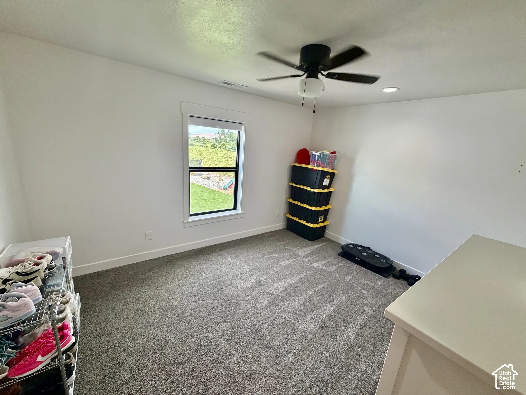 Bright room featuring a window with exterior views, neutral carpet, and a ceiling fan with integrated lighting