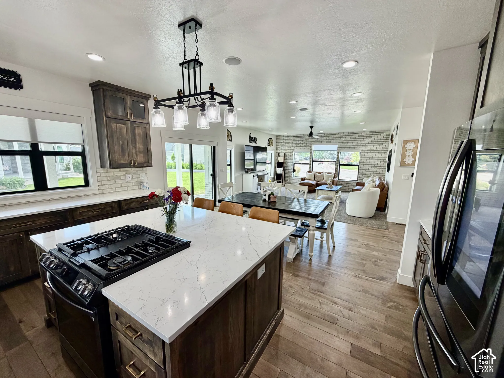 Open-concept kitchen featuring a large island with a built-in range, white stone countertops, dark wood cabinetry, and wood-finish flooring