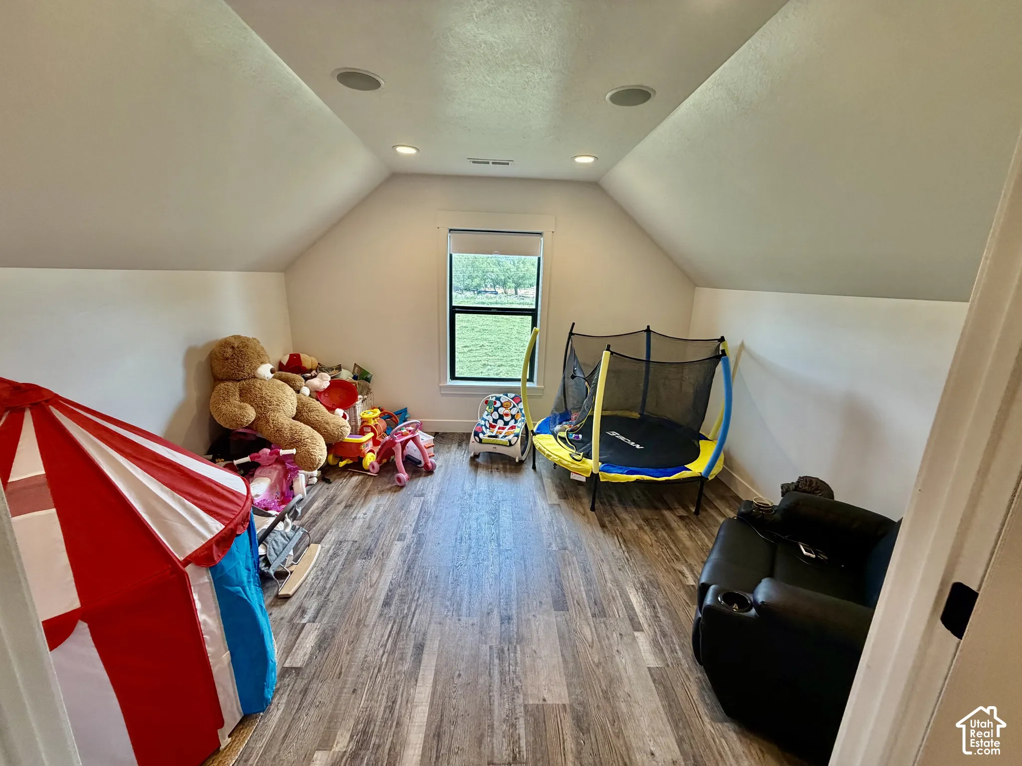 Attic space featuring wood-finish flooring, a single window, recessed lighting, and sloped ceilings