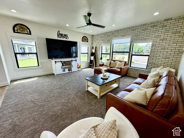 Spacious living area featuring a light-colored brick accent wall, recessed lighting, a ceiling fan, and large windows with black frames