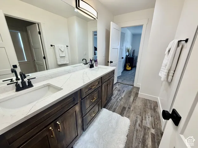 Double vanity featuring black fixtures, a white countertop with grey veining, wood-finish cabinetry, and a large wall mirror