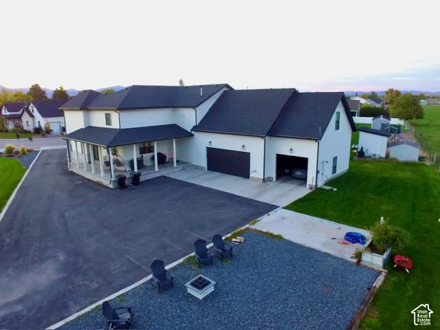 White exterior with a dark roof, covered porch, attached garage, and paved driveway