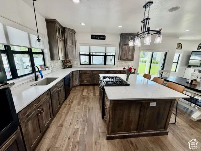 Expansive kitchen featuring a large central island with seating, a gas range, wood-finish flooring, white countertops, and dark wood cabinetry