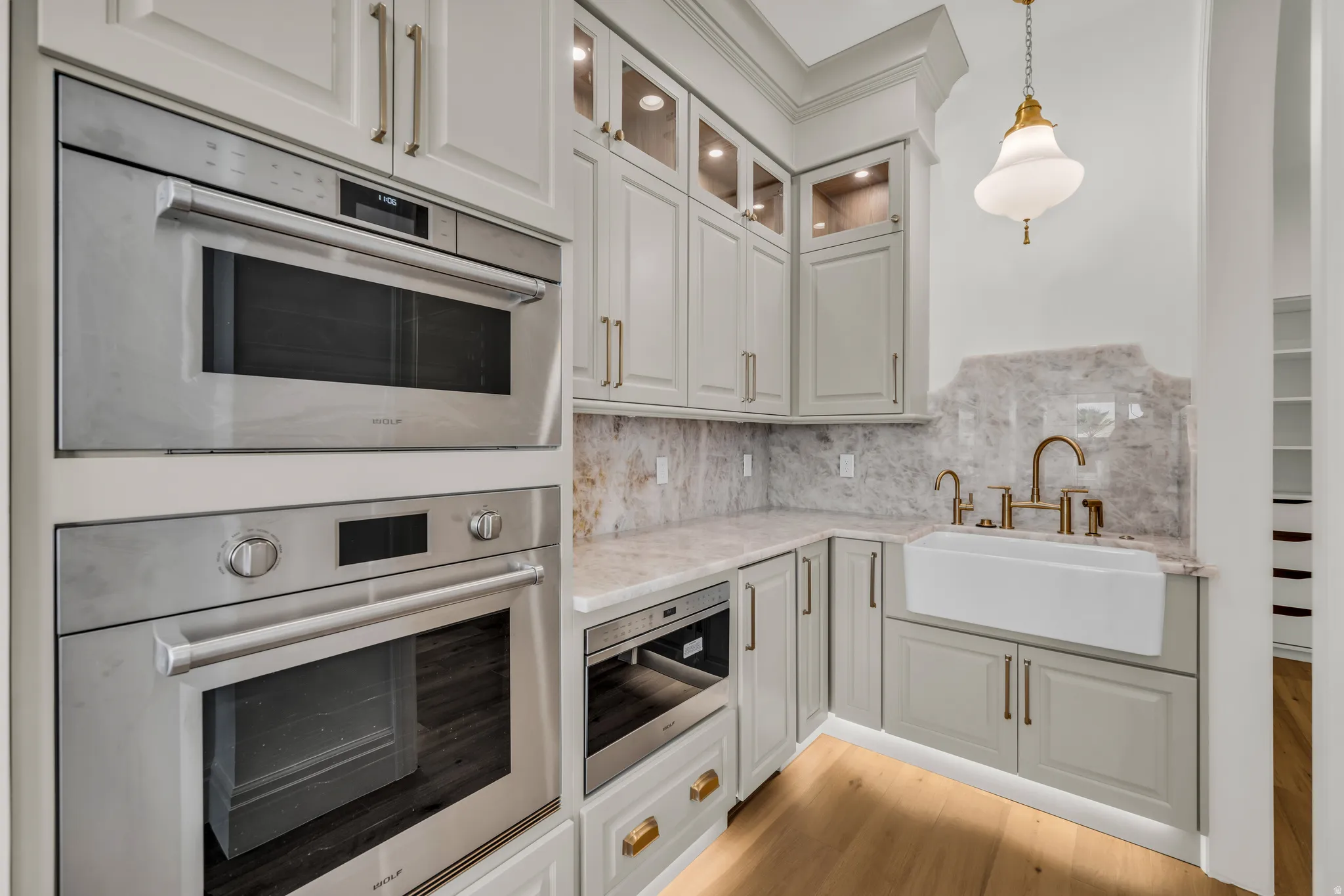 Gourmet kitchen with double wall ovens, built-in microwave, farmhouse sink, and elegant light-toned cabinetry with brass hardware