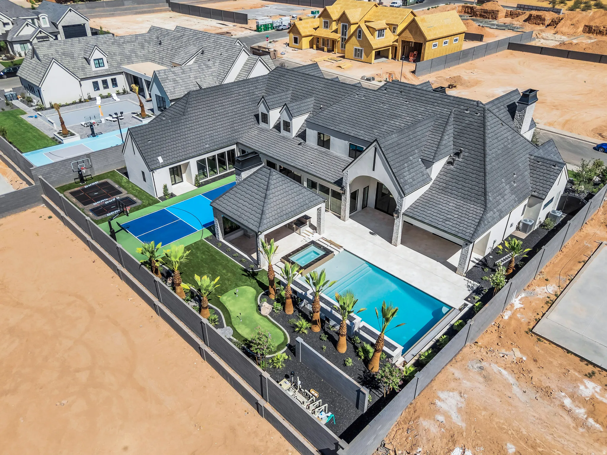 Expansive backyard oasis featuring a swimming pool, integrated spa, covered patio, sport court, putting green, and mature palm trees