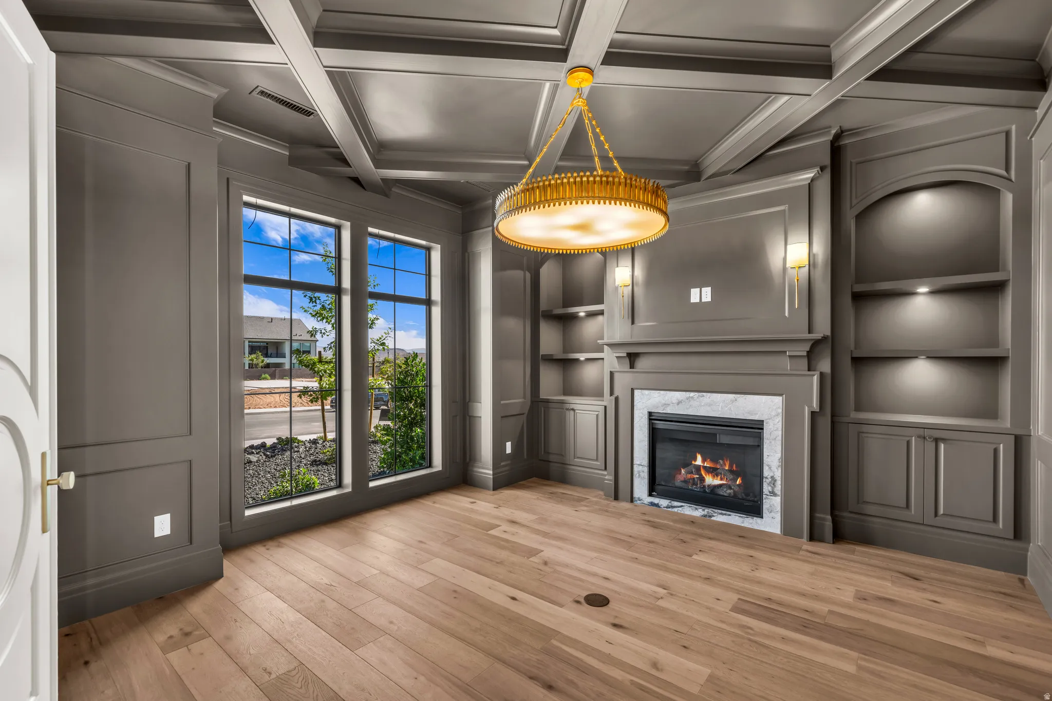 Coffered ceiling with a central chandelier, complemented by recessed lighting and wall sconces