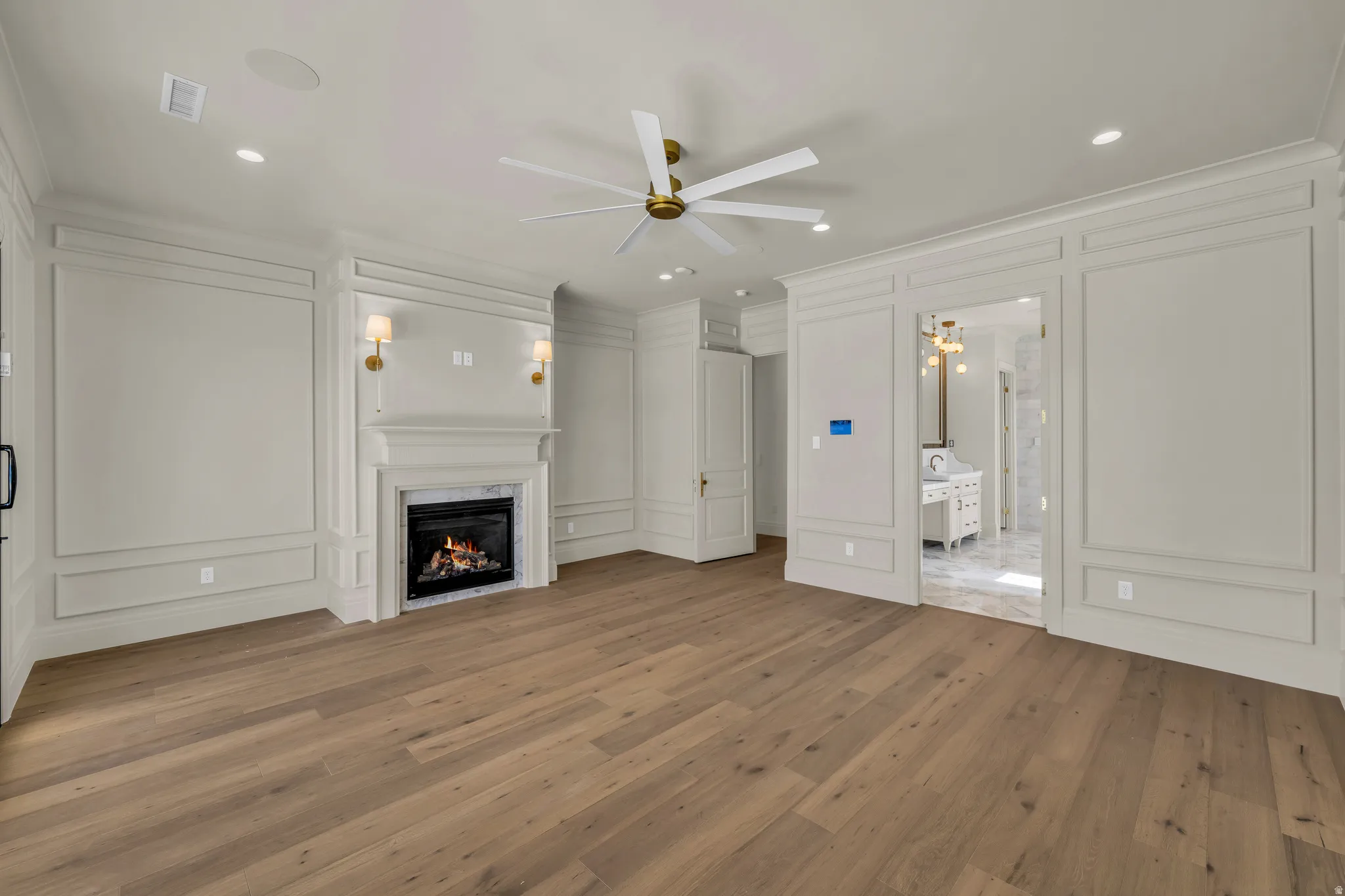 Spacious room featuring wood-finish flooring, an ornate fireplace with sconce lighting, extensive wall paneling, and a ceiling fan