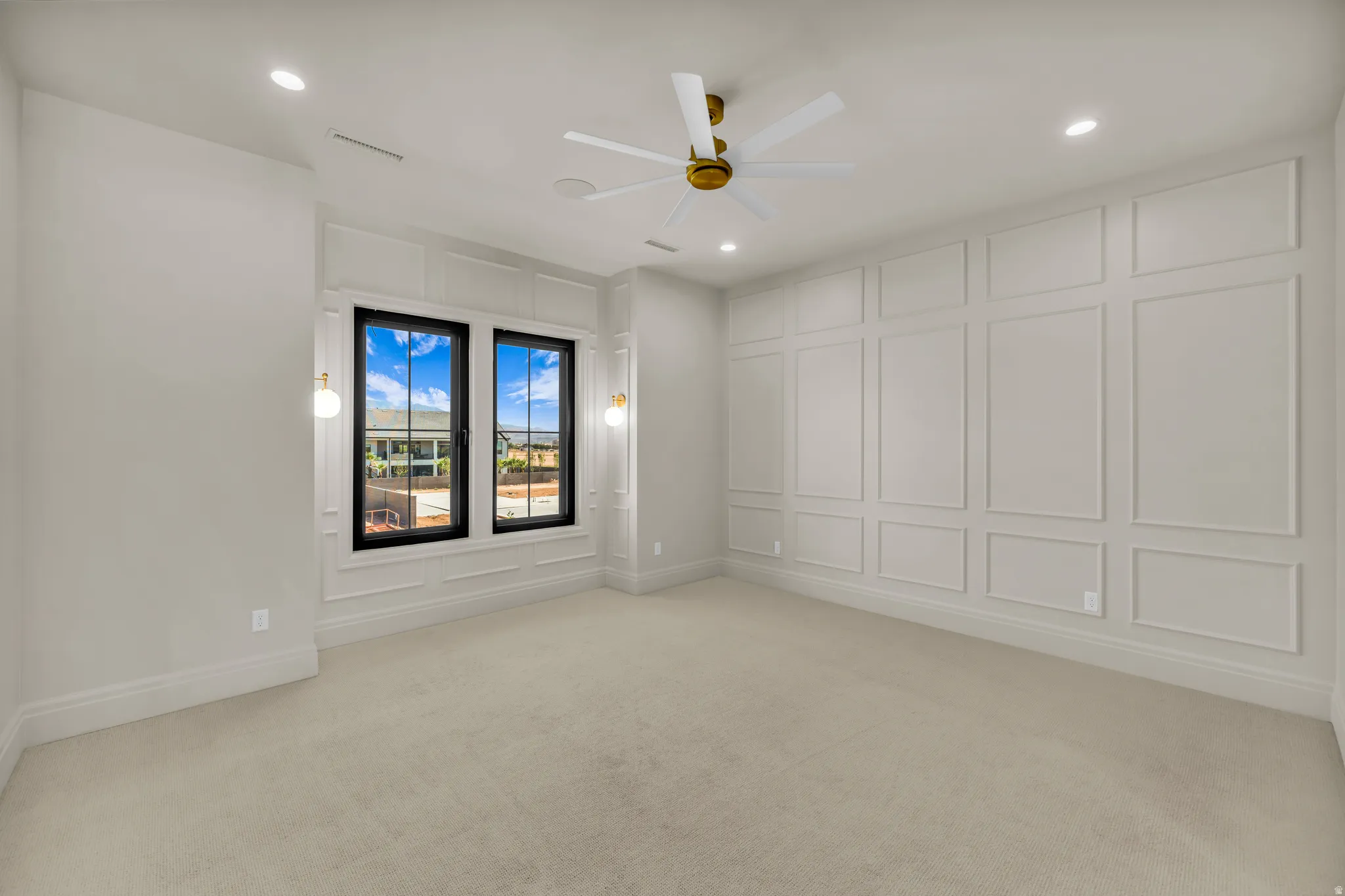 Spacious interior room featuring extensive decorative wall paneling, light-toned carpeting, and a ceiling fan with gold-tone accents
