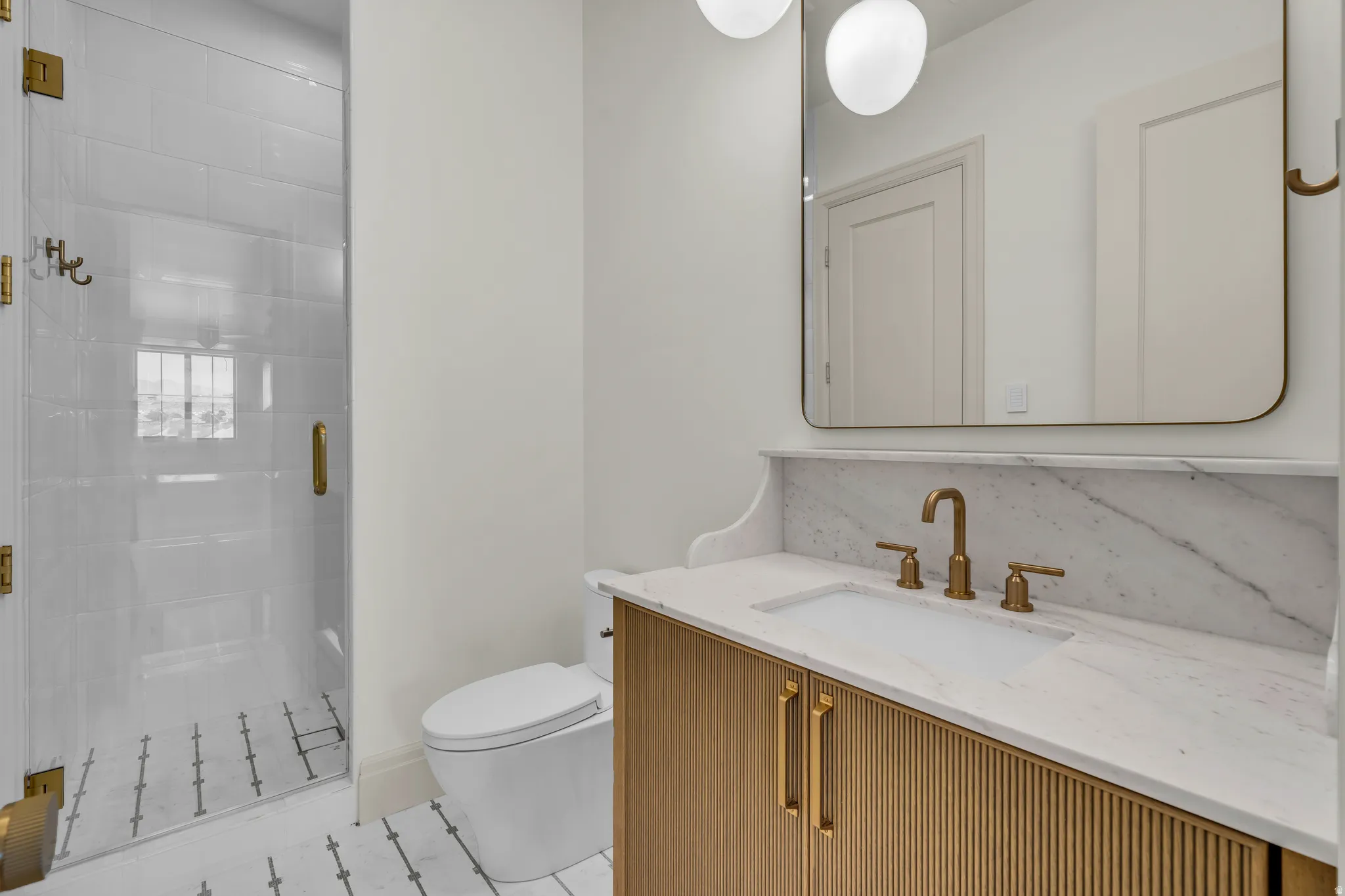 Modern bathroom featuring a glass-enclosed shower with white subway tile, a vanity with a fluted wood-finish front, and a white countertop with integrated sink