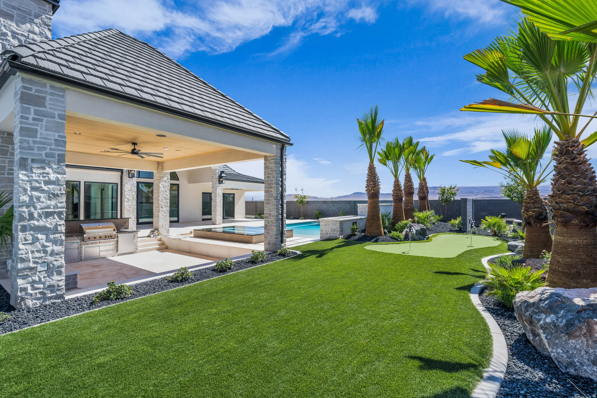 Expansive exterior showcasing a covered patio with built-in grill, a putting green, mature palm trees, and a swimming pool with an integrated spa