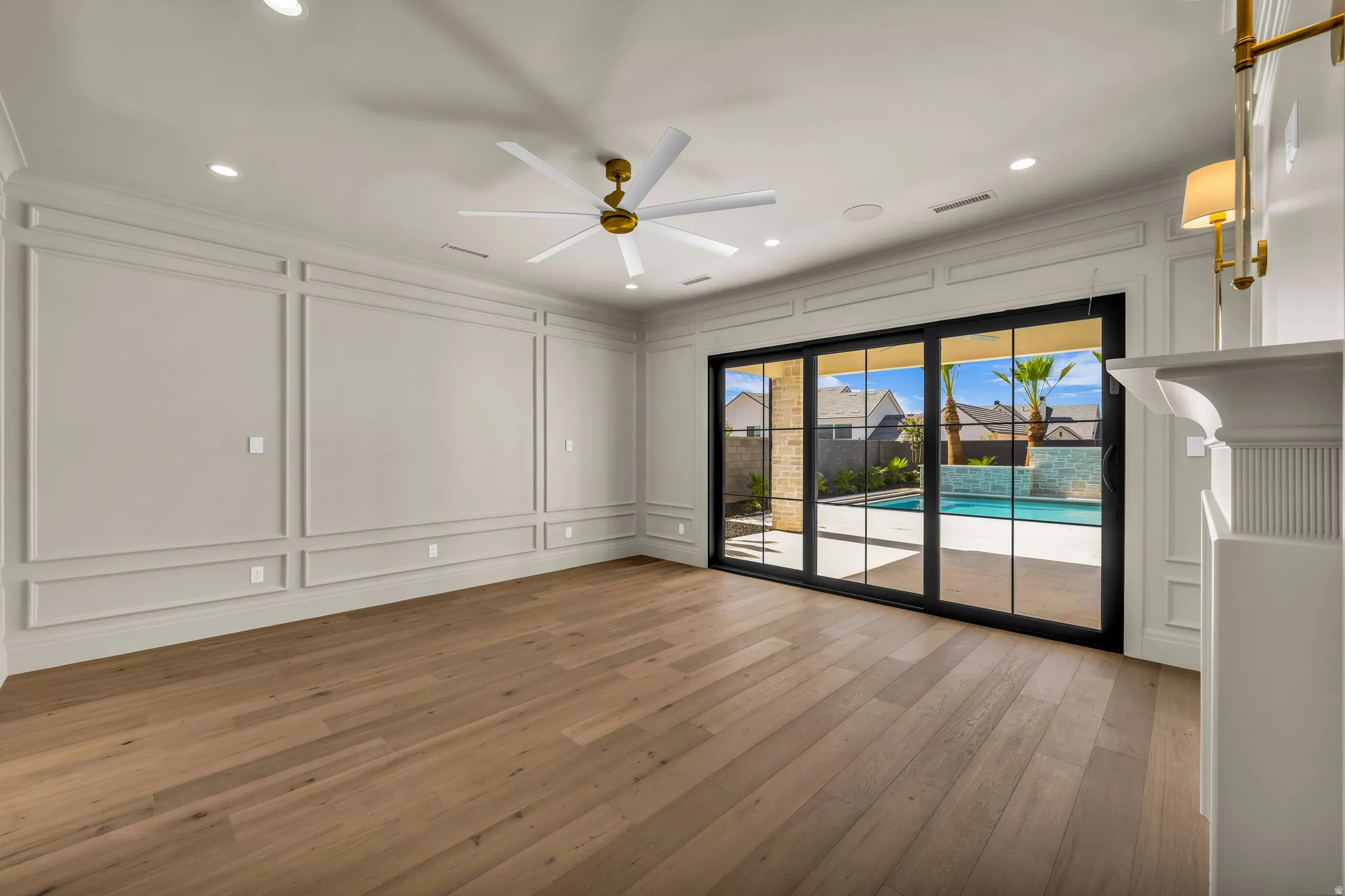 Spacious room featuring wood-finish flooring and extensive wall paneling, complemented by a contemporary ceiling fan with gold-tone accents