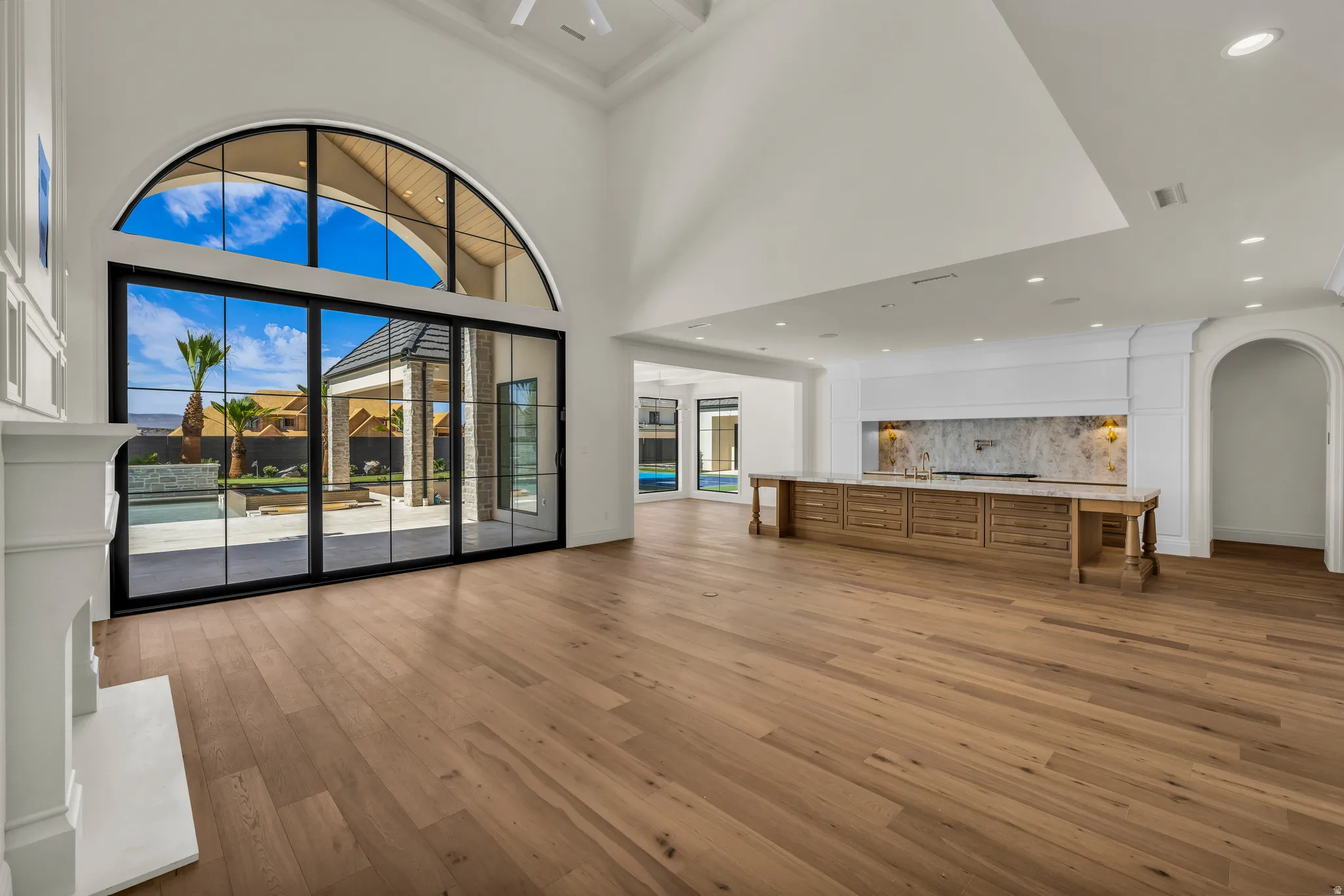 Expansive room featuring high vaulted ceilings, light wood-finish flooring, and a white fireplace mantel