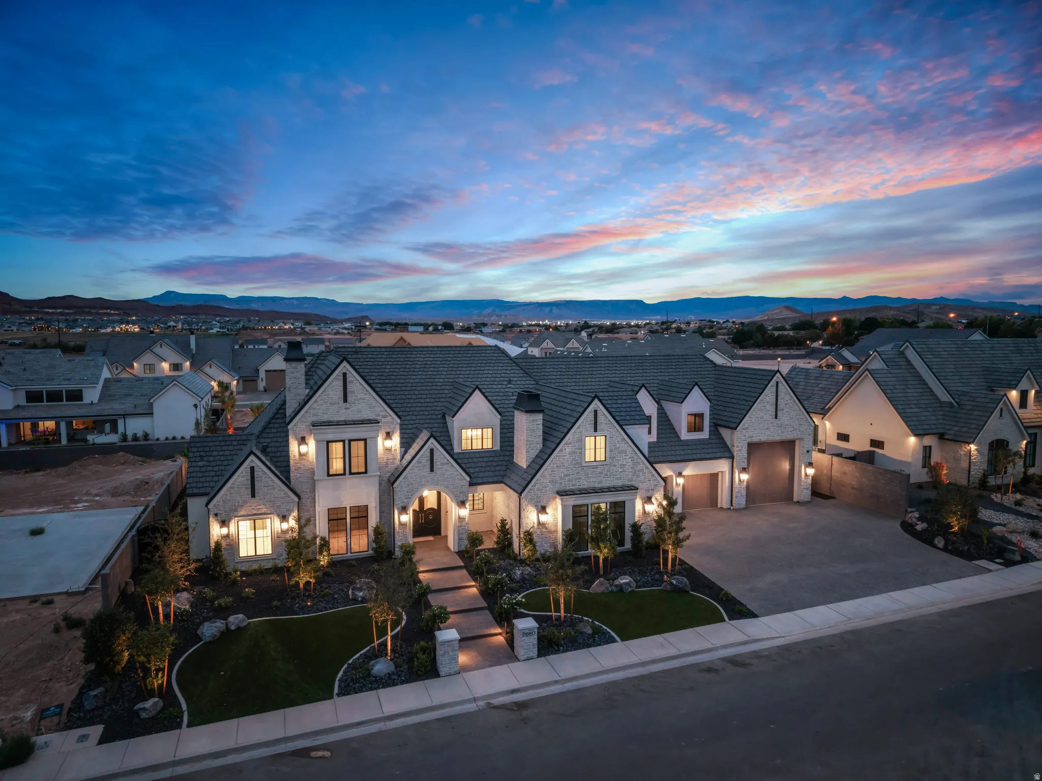 Grand residence featuring a stone and stucco exterior, prominent gabled rooflines, an inviting entryway, a paved driveway, and established front landscaping