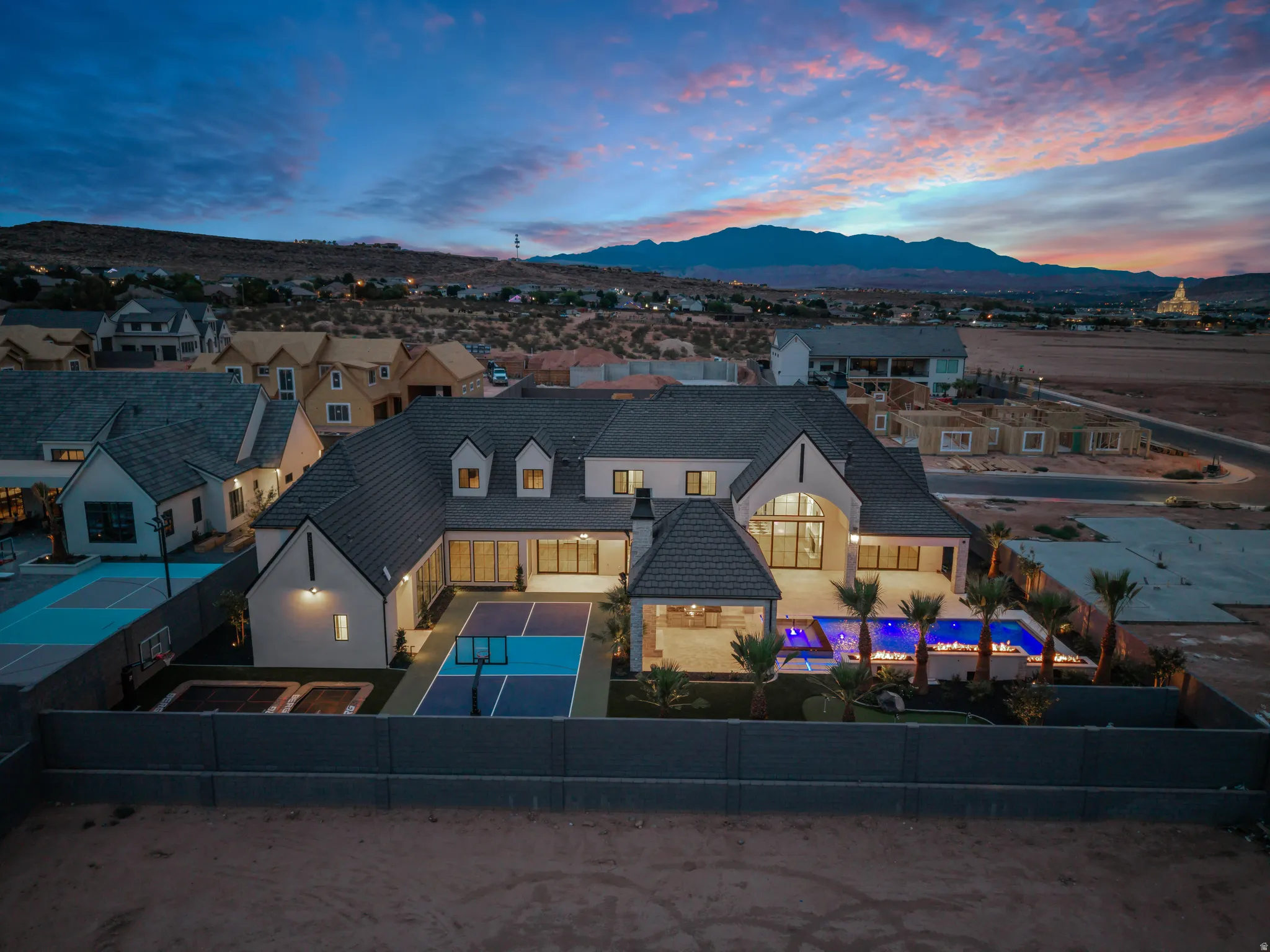 Contemporary residence featuring a dark tile roof, multiple dormer windows, a spacious backyard with a lighted pool, an outdoor covered patio, and a dedicated sport court