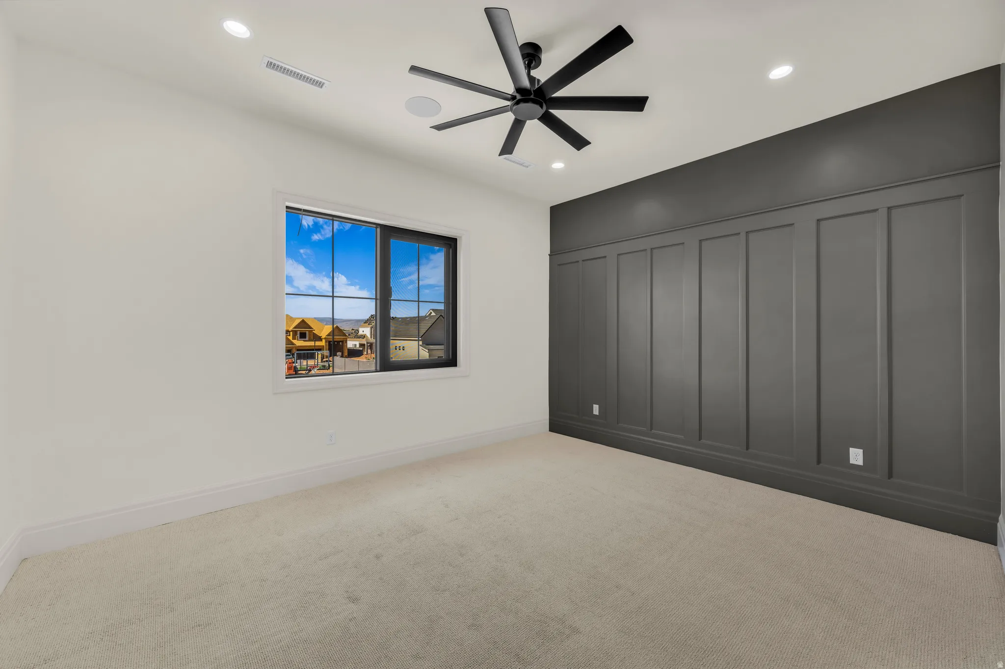 Neutral carpeted room featuring a dark accent wall with wainscoting detail