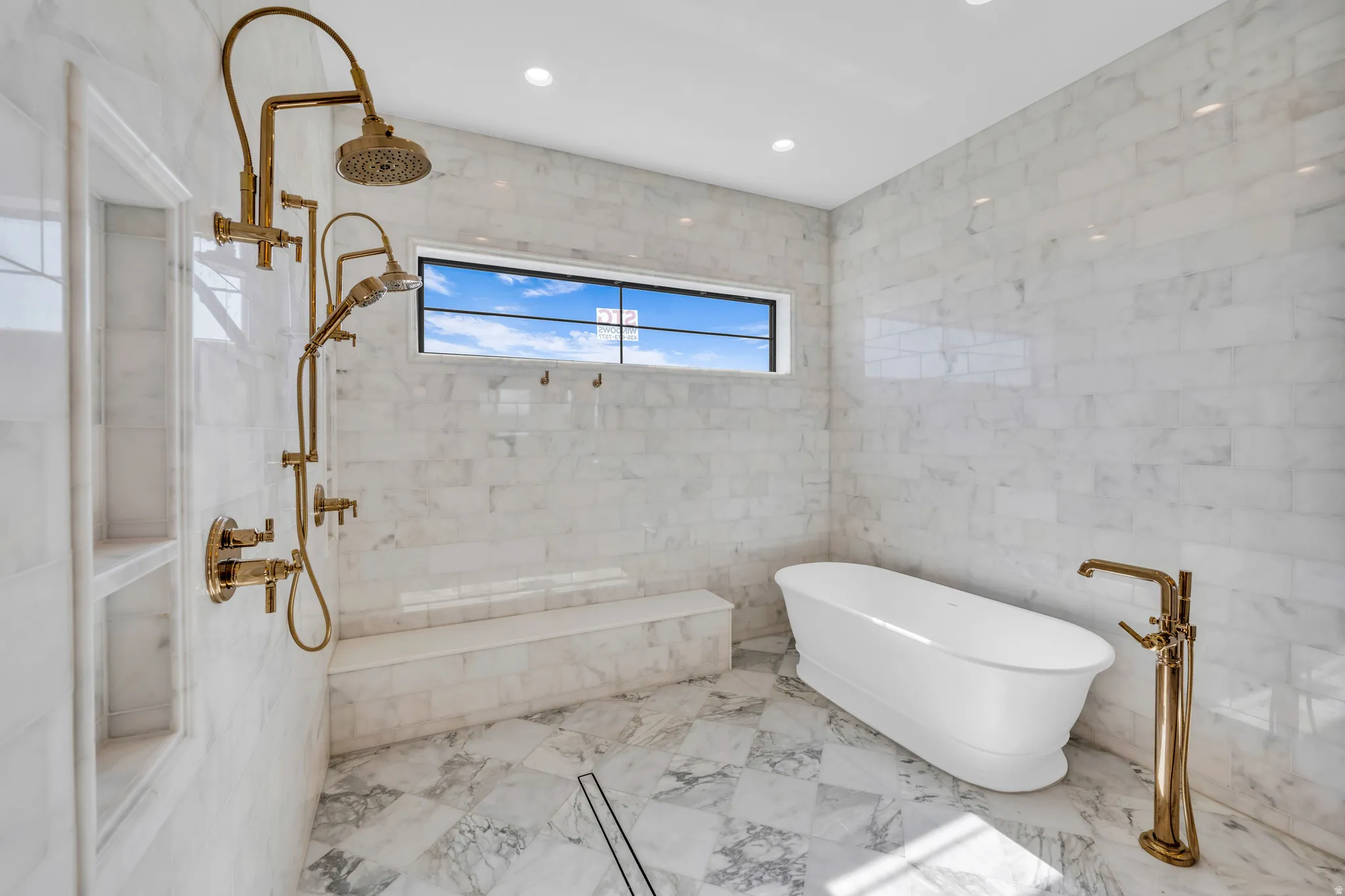 Luxurious bathroom featuring a freestanding soaking tub, a multi-function shower system with a rain shower head, a built-in shower bench, marble-finish wall and floor tiling, and a transom window