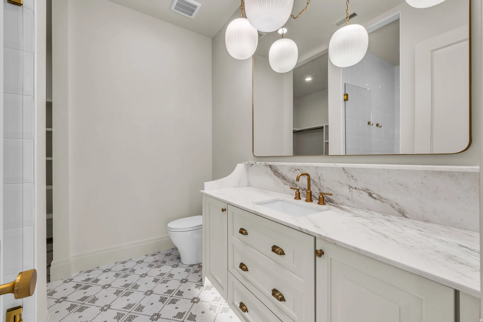 White vanity with an integrated sink, polished brass hardware, and a stone countertop extending to a full-height backsplash