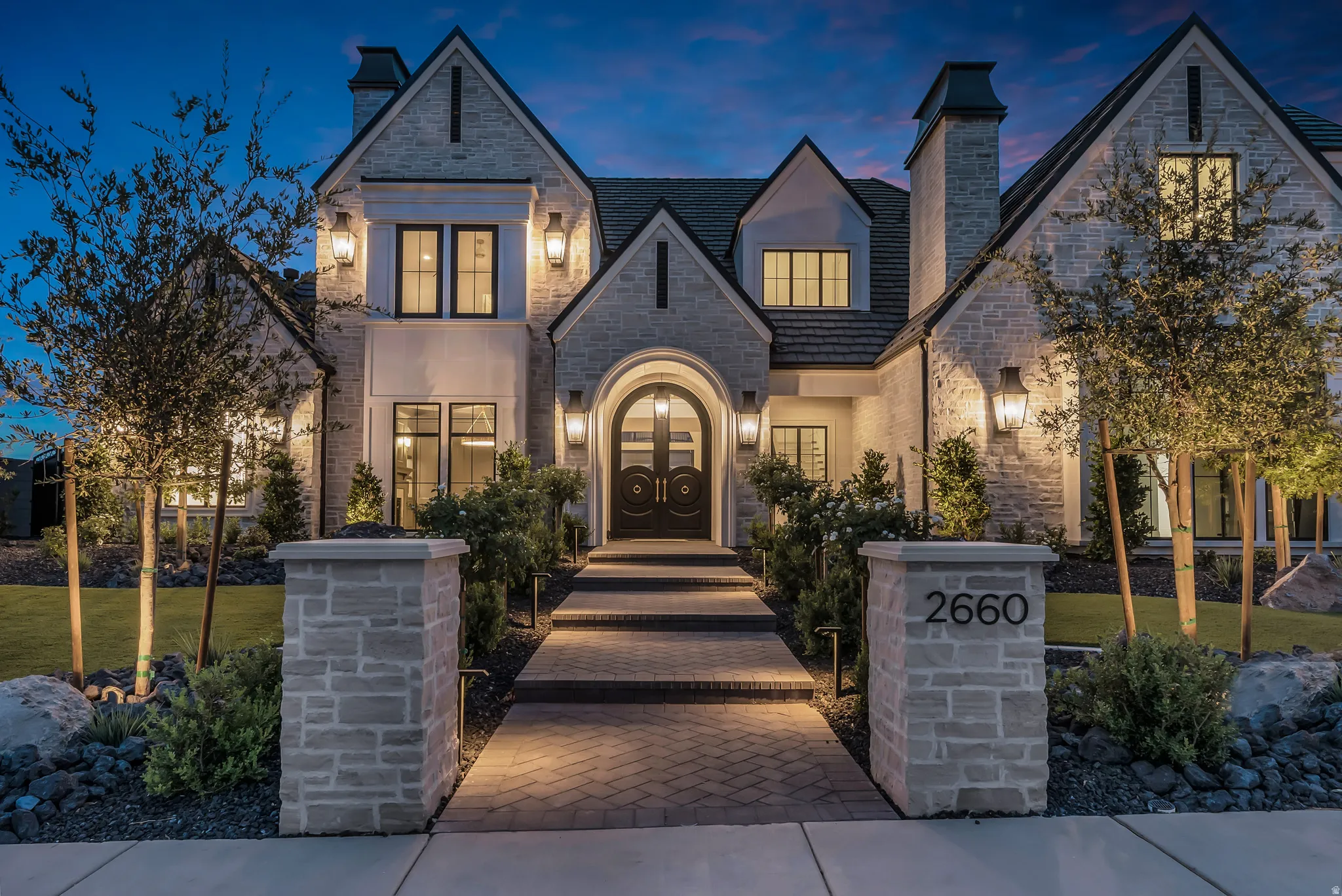 Stone facade residence featuring a grand arched entry with double doors, multiple gables, and prominent chimneys