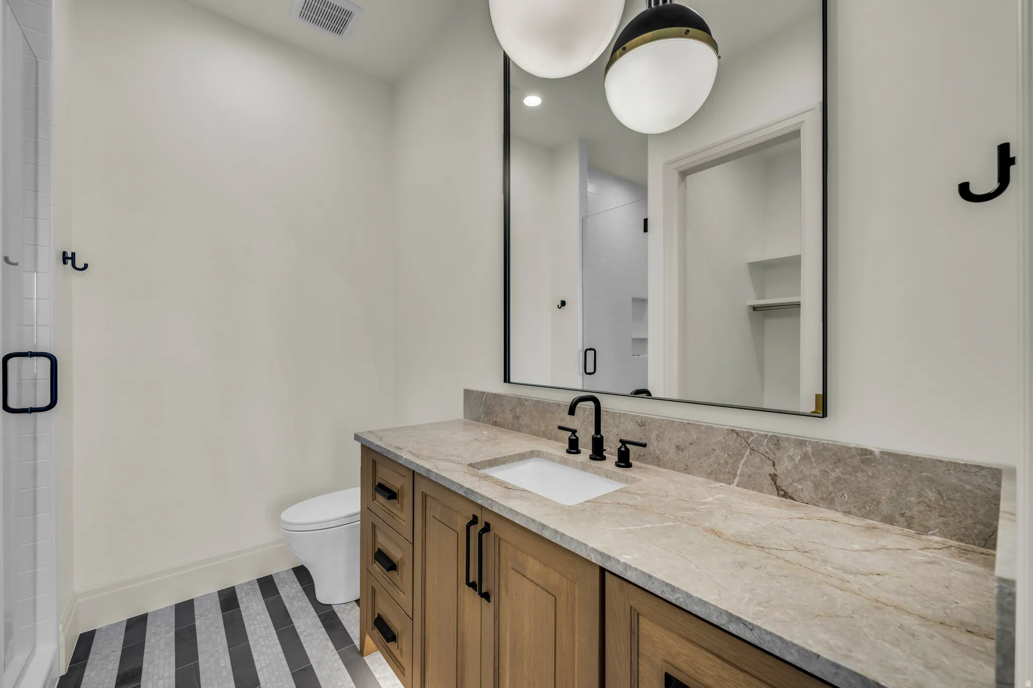 Bathroom featuring a wood-finish vanity with a stone countertop, an undermount sink, and matte black fixtures